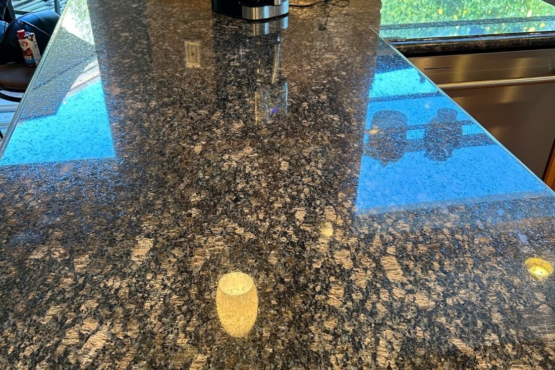 A polished granite kitchen countertop in Newport Beach adjacent to the repaired section, showcasing a smooth, reflective finish with rich natural patterns.